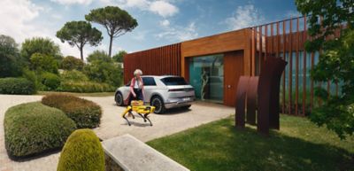 A person walking around the back of an all-electric Hyundai IONIQ 5 next to a house.