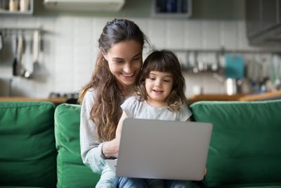 Matka i córeczka siedzą na zielonej kanapie i wspólnie korzystają z laptopa.