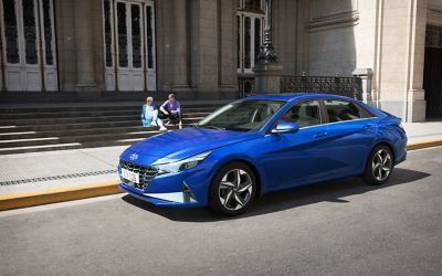 Niebieski Hyundai Elantra stoi zaparkowany na ulicy, a obok na schodach siedzi para ludzi.