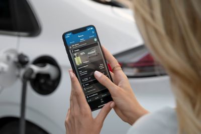 Una mujer mira el estado de su Hyundai IONIQ desde su teléfono mientras carga su coche.