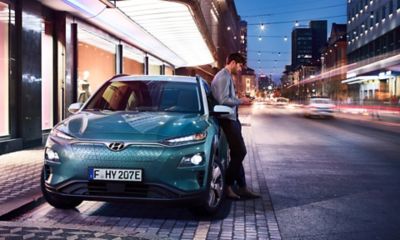 Un homme s'appuie sur un Hyundai KONA Electric dans le centre-ville.