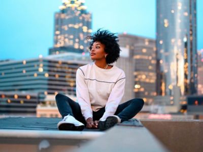 A woman sitting in front of a city skyline enjoying the reduced urban noise due to EV mobility.
