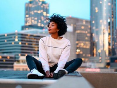A woman sitting in front of a city skyline enjoying the reduced urban noise due to EV mobility.