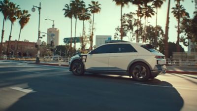 The all-electric Hyundai IONIQ 5 robotaxi driving down a street lined with palm trees.