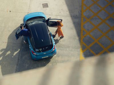 View from above, a couple is getting into their blue Hyundai i10.