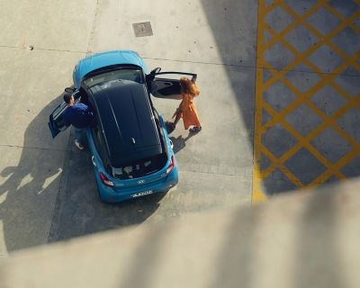 View from above, a couple is getting into their blue Hyundai i10.