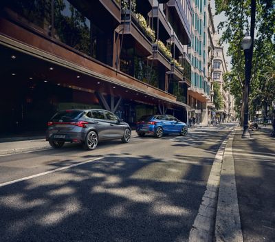 Zwei Hyundai i20 parken hintereinander in einer städtischen Wohn- und Geschäftsstraße. 