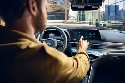 Un hombre en el asiento del conductor controlando la pantalla táctil del nuevo Hyundai i20.