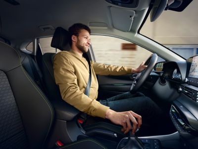Muž ve světle hnědém tričku s dlouhými rukávy řídící nový Hyundai i20, z pohledu spolujezdce