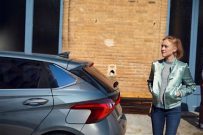 a young woman standing behind an Hyundai i20, left side view