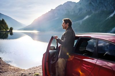Uomo guarda un lago mentre si appoggia alla portiera di Nuova Hyundai i30 Wagon