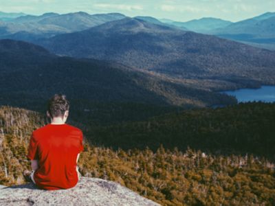 Persona sentada en la cima de una montaña mirando al horizonte.