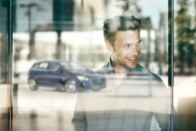 Persona sonrie a través de la ventana que refleja un vehículo Hyundai.