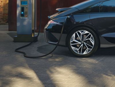 A woman plugging her Hyundai IONIQ 5 electric vehicle to a charging station.