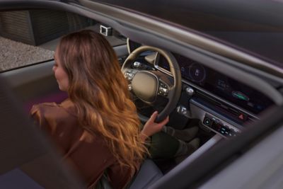 A woman inside the Hyundai IONIQ 6 with one hand on the steering wheel putting on the seat belt