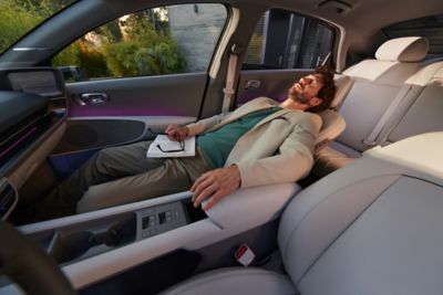 Hombre con traje blanco y camiseta verde tumbado en el asiento ajustable del Hyundai IONIQ 6.