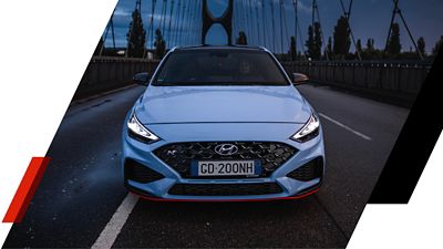 The Hyundai i30 N on a bridge with bright front lamps.