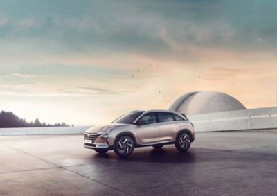 The all-new Hyundai Nexo, shown from the side, standing before a futuristic building at sunset.