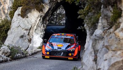Hyundai Motorsport driver Oliver Solberg's i20 N WRC Rally1 driving on a mountain road. 