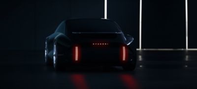 Die Sillhouette eines Hyundai IONIQ Konzeptfahrzeugs in dunkler Kulisse mit eingeschaltetem Licht. 