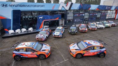 The Hyundai Rally2 cars lined up in front in a parking lot.