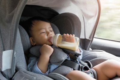 Baby zuigt op een fles, met gordel vastgemaakt in kinderzitje.