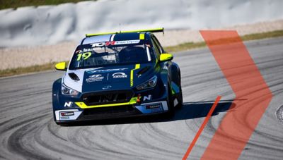 A picture of Hyundai Motorsport’s i30 VELOSTER N TCR in action on a racetrack shown from the front.