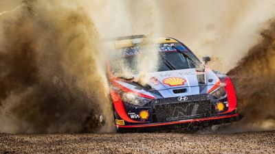The Hyundai i20 N WRC rally race car churning through gravel on course.