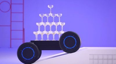 MobED (Mobile Eccentric Droid) se pohybuje po překážce při přepravě naskládaných sklenic na šampaňské