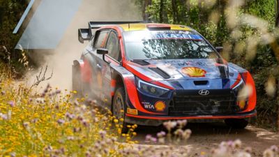 The Hyundai i20 N WRC rally race car speeding down a road through the woods.