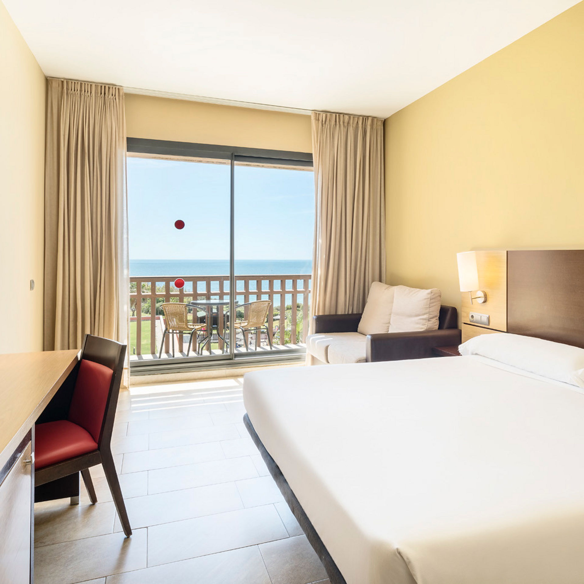 amplia habitación accesible con cama doble, sofá, escritorio, televisión y terraza con vistas al mar
