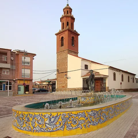 Fuente ornamental en plaza urbana con torre de iglesia al fondo
