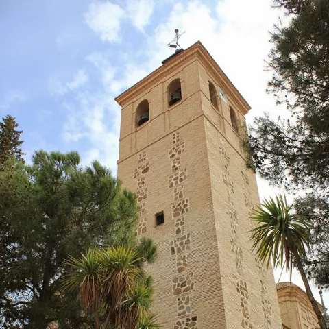 Campanario de iglesia de ladrillo rodeado de vegetación