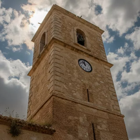 Torre campanario con reloj bajo cielo nublado