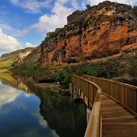 Pasarela de madera junto a río y acantilados