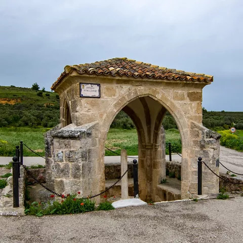 Pequeño templete de piedra con arcos y tejado de tejas en entorno rural.