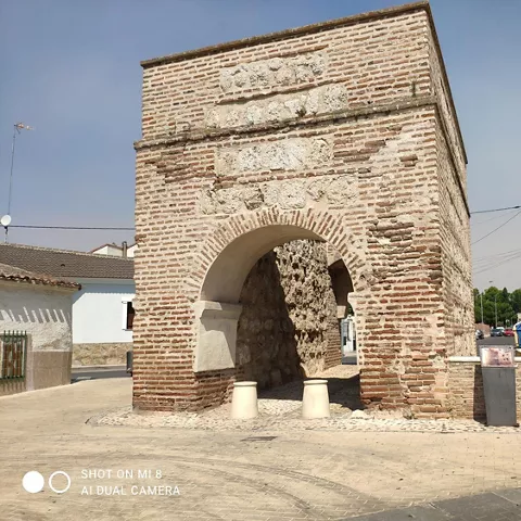 Arco de ladrillo con fuente y pavimento peatonal en entorno urbano.
