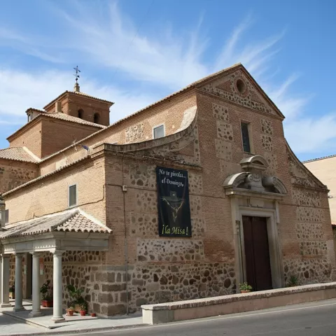 Iglesia de ladrillo con pórtico y ciprés junto a la fachada