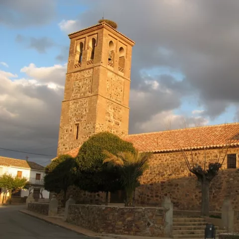 Iglesia de Arroba de los Montes construida en piedra, con torre campanario cuadrada y plaza con fuente.