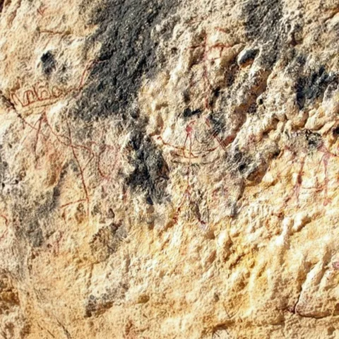 Detalle de pared rocosa con grabados y trazos rojizos muy desgastados.