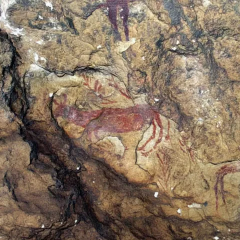 Pintura rupestre de ciervo en rojo sobre roca irregular.