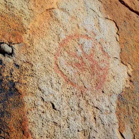 Símbolo circular pintado en rojo sobre superficie rocosa.