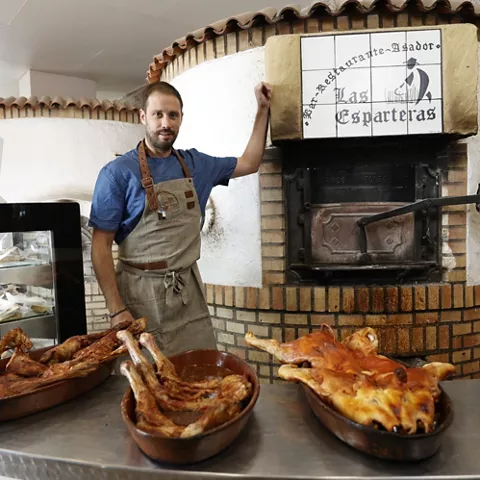 Cocinero junto a horno tradicional con bandejas de carne asada.