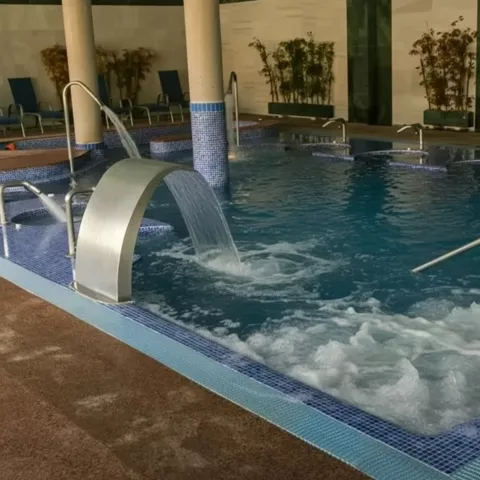 Piscina de hidromasaje interior con chorros de agua y columnas revestidas de azulejo.
