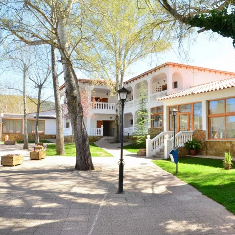 Patio ajardinado con edificios blancos, grandes ventanales y camino con farolas.