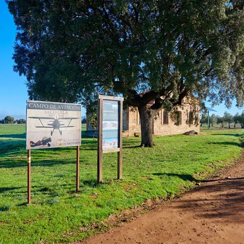 Carteles informativos junto a camino rural y construcción tradicional