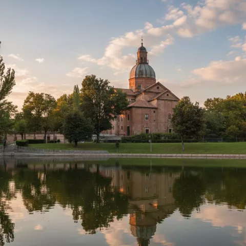 Templo de ladrillo y cúpula reflejado en un estanque rodeado de árboles.