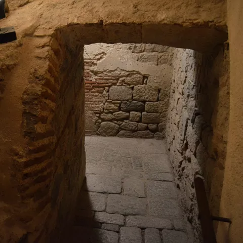 Pasillo subterráneo con muros de piedra y suelo empedrado.
