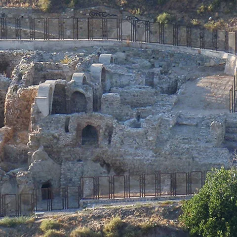 Ruinas de antiguos baños junto al río con arcos restaurados y pasarelas metálicas.