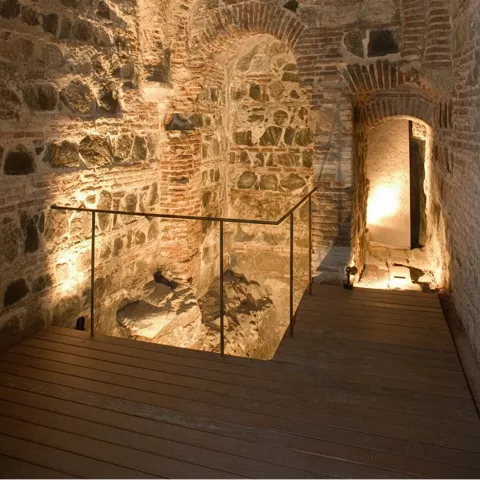 Espacio subterráneo iluminado con arcos y muros de mampostería.